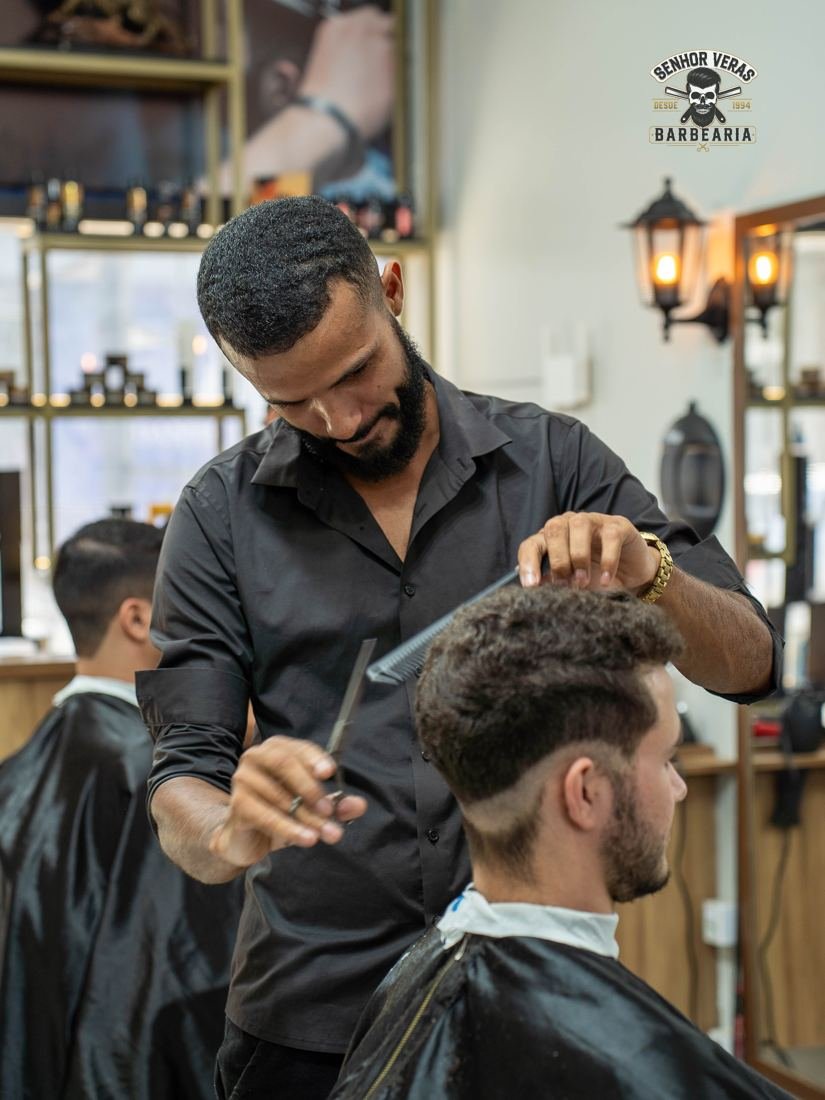 Barbeiro finalizando um corte degradê com pente e tesoura